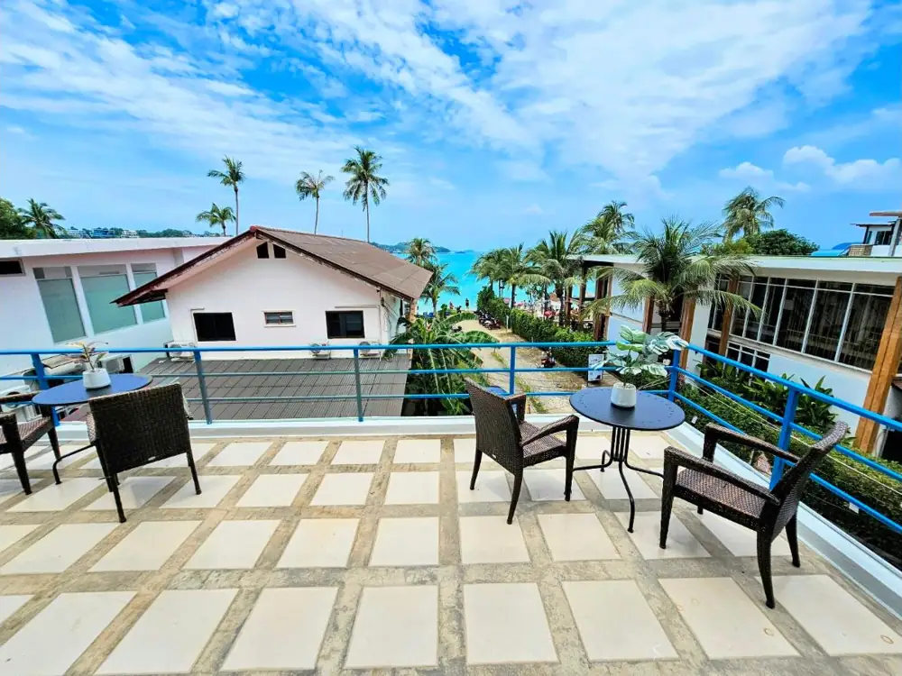 Penthouse rooftop patio with tables and chairs looking over palm trees to the turquoise bay